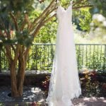 A detailed wedding dress hanging from a tree in a garden.