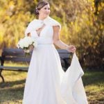 A wedding portrait of a bride in a white wedding dress standing in a park.