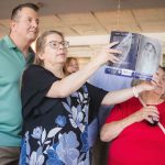 A group of people celebrating at a birthday party, looking at a photo of a baby.