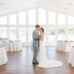 A candid wedding preparation moment with a bride and groom in a large room with windows.