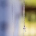 A silver cross pendant on a wedding chain.