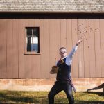 A man throwing a frisbee during a wedding ceremony in front of a barn.