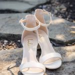 A pair of white wedding sandals sitting on a rock.