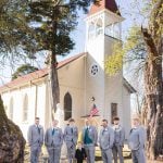 A group of groomsmen posing in front of a church for a wedding portrait.