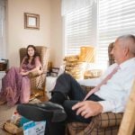 A couple sitting candidly in a cozy living room chair during wedding preparation.