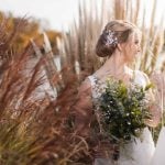 A bride in a wedding dress posing for a portrait amidst tall grass.