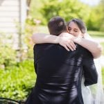 A candid bride and groom hugging in front of a house as part of their wedding preparations.