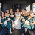 A group of bridesmaids in candid wedding preparation sitting on the back of a limo.