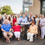 A group of people celebrating a birthday in front of a building.