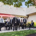 A group of groomsmen posing in front of a tree for a wedding portrait.