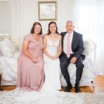 A candid wedding photo captures a bride and her parents during wedding preparation.