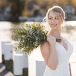 A wedding portrait of a bride holding a bouquet on a dock.