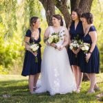 The bride and her bridesmaids are posing for a wedding portrait under a tree.