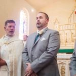 Groom and groomsmen participating in a wedding ceremony with a priest.