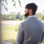 A groom in a suit is looking out of a window during wedding preparation.