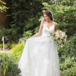 A bride in a white wedding dress posing for a portrait in a garden.