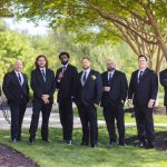 A group of groomsmen posing in front of a tree at a wedding.