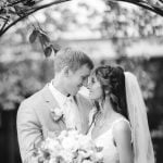 A black and white portrait of a bride and groom at their wedding ceremony in front of an arch.