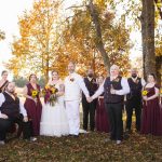 A group of bridesmaids and groomsmen posing for a wedding portrait in the fall.