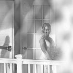 A black and white photo of a bride during her wedding ceremony on a porch.