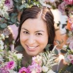 A woman smiles in front of a bunch of flowers for her wedding portrait.