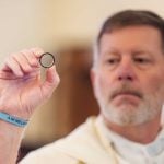 A priest is performing a wedding ceremony, holding a black ring in his hand.