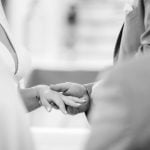 A bride and groom during their wedding ceremony, holding hands.