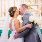 A couple exchanging a ceremonial kiss outside of a church during their wedding.