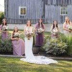 A wedding party poses in front of a barn for a portrait.