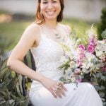 A bride sitting on a bench holding a bouquet for her wedding day portrait.