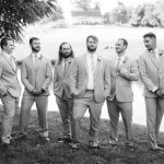 A group of groomsmen posing for a wedding portrait next to a pond.