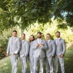 A group of groomsmen posing for a wedding portrait in front of a tree.