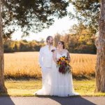 A wedding portrait of a bride and groom standing next to trees in a field.