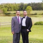 Two men in tuxedos posing for a wedding portrait.