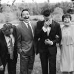 A black and white wedding portrait of a group of people laughing.