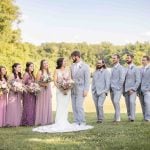 A group of bridesmaids and groomsmen posing for a wedding portrait in a field.