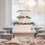 A detailed white wedding cake with greenery on top.