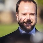 A man in a suit and tie is smiling at a wedding ceremony.