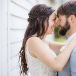 A bride and groom embracing in front of a white house for their wedding portrait.