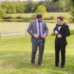 Two men in tuxedos standing in a field for a portrait.