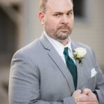 A man in a suit and tie standing in front of a house for a wedding portrait.