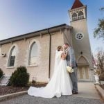 A wedding couple kiss in front of a church.