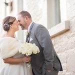 A bride and groom kissing during their wedding portrait session in front of a stone wall.