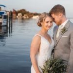 A wedding portrait of a bride and groom standing on a dock.