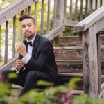 A man in a tuxedo sitting on a set of stairs for a wedding portrait.