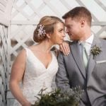 A wedding couple embracing in front of a gazebo.