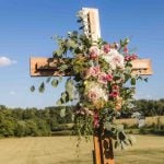 A wooden cross adorned with flowers and greenery in a field.