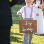 A little boy participating in a wedding ceremony, holding a sign that says ring security.