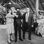 A bride and groom kiss during their rustic wedding ceremony in a barn.