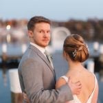 A wedding portrait of a bride and groom on a dock at dusk.